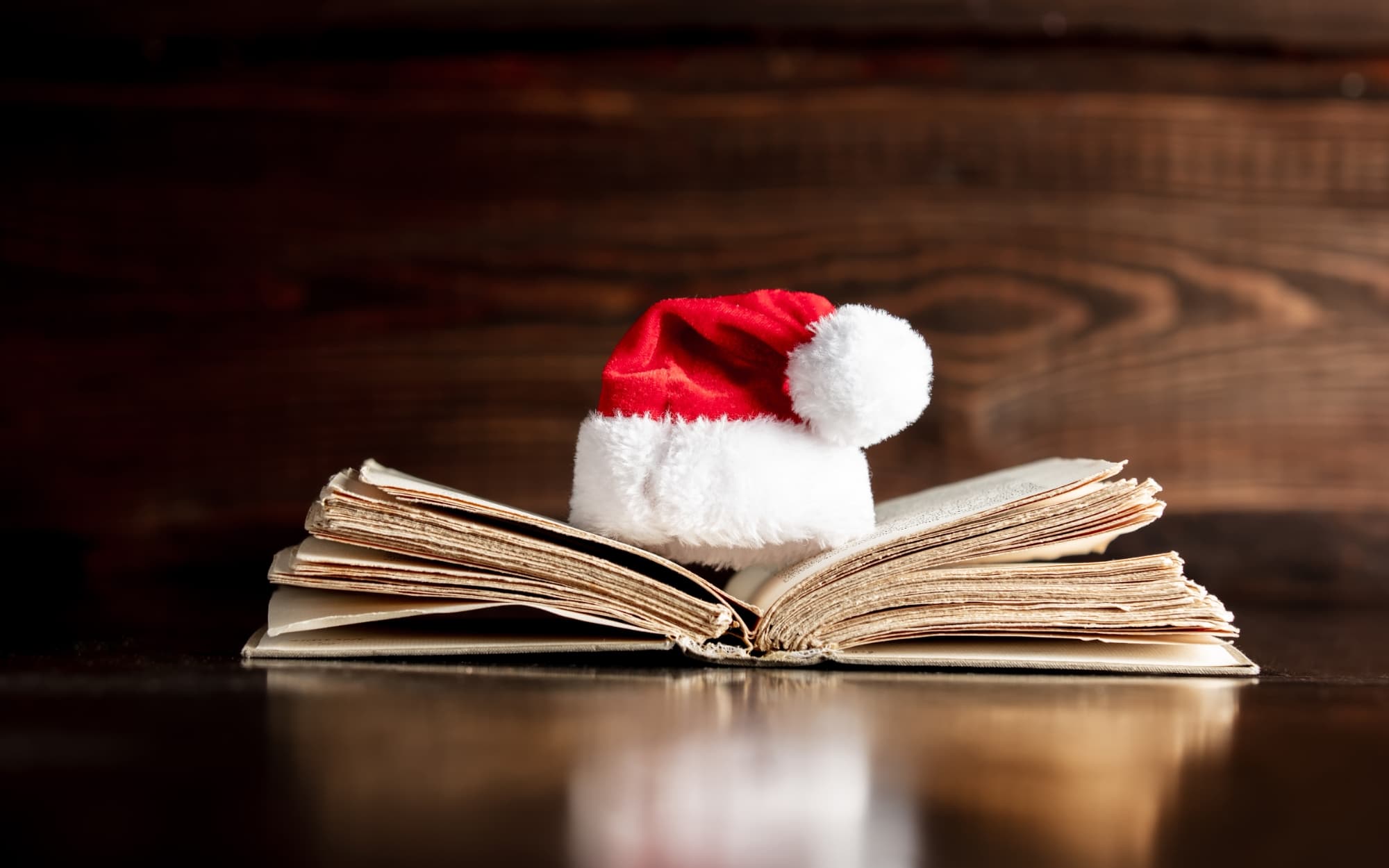 A book sits open on a table, containing a Christmas story. A Santa hat rests on top of it.