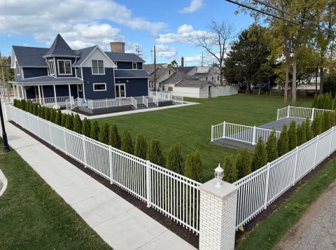 The large green space in front of the Barker Cottage is surrounded by a white fence.