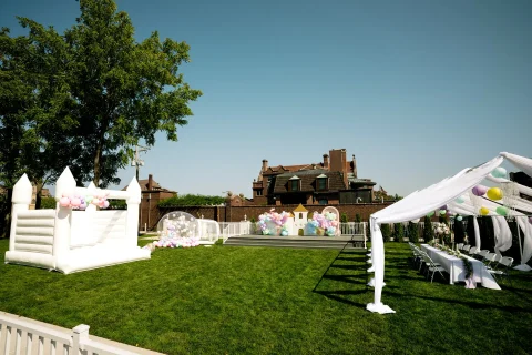 The green space at the Barker Cottage with outdoor seating. Configured for a child's party, with a white bouncy house, balloons, and a castle.