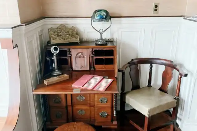 A tiffany lamp of top of a desk with an antique phone.
